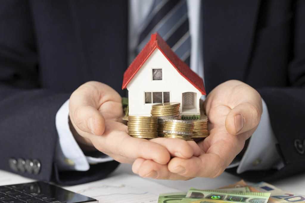 pessoa segurando miniatura de casa e moedas, representando o processo para investir em imóveis